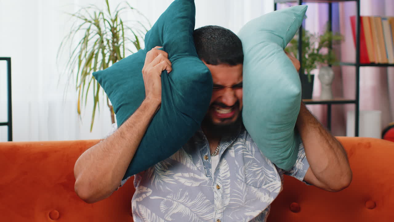 Neighbors repair work irritated man by loud music at home cover ears with pillows annoyed by noise
