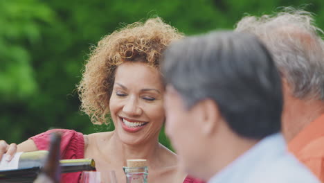 woman filling wine glass at drinks party for senior friends in garden at home