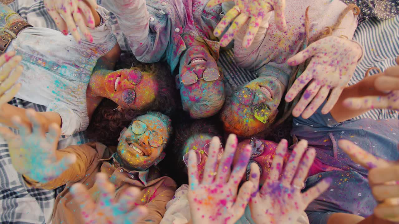 Top view portrait of cheerful youth with dirty faces stretching arms covered with gulal paint having fun at Holi party
