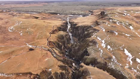 Stunning drone view of Fjaðrárgljúfur Canyon in Iceland, volcanic cliffs, winding river and vast scenic highlands during winter thaw.