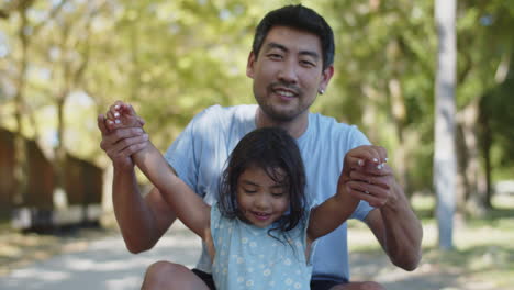 happy asian father and daughter sitting with outstretched arms and moving