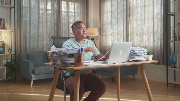 Fat Asian Man Having Video Call On Laptop While Working With Documents At The Office
