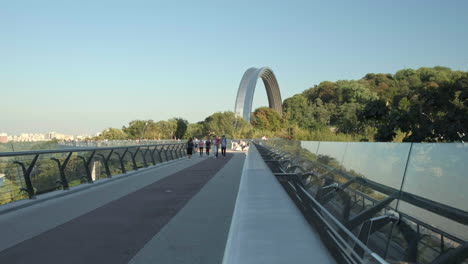 slider shot of people walk across the glass bridge in kiev on a warm autumn evening. the friendship arch is behind