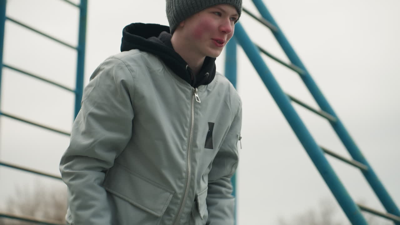 A young boy performs a workout, moving up and down with a smile on his face, he is exercising near an iron pole