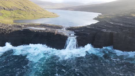 wide drone footage of the bøsdalafossur waterfall near the leitisvatn lake, aka the floating lake, on the vagar island in the faroe islands