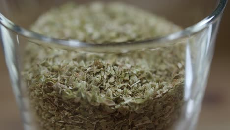 dried oregano leaves in a small transparent container, mashed with a spoon