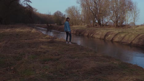 girl standing thoughtful at a river in a forrest - slowmotion