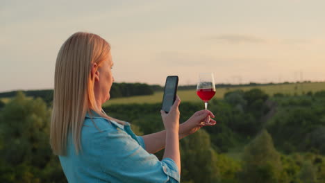 Eine-Bloggerin-Fotografiert-Ein-Glas-Wein-Vor-Der-Kulisse-Eines-Malerischen-Tals,-In-Dem-Die-Sonne-Untergeht