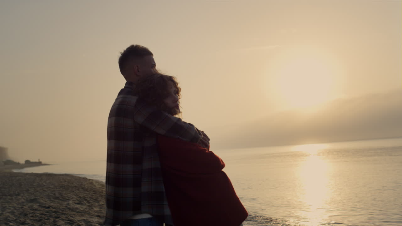 Gün doğumunda sahilde duran romantik kadın ve erkek. Çift deniz manzarasının keyfini çıkarıyor.