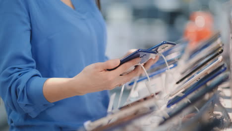 Close-up-of-a-woman-holding-two-new-smartphones-in-her-hands-and-choosing-the-best-phone-model-in-the-modern-electronics-store-to-buy