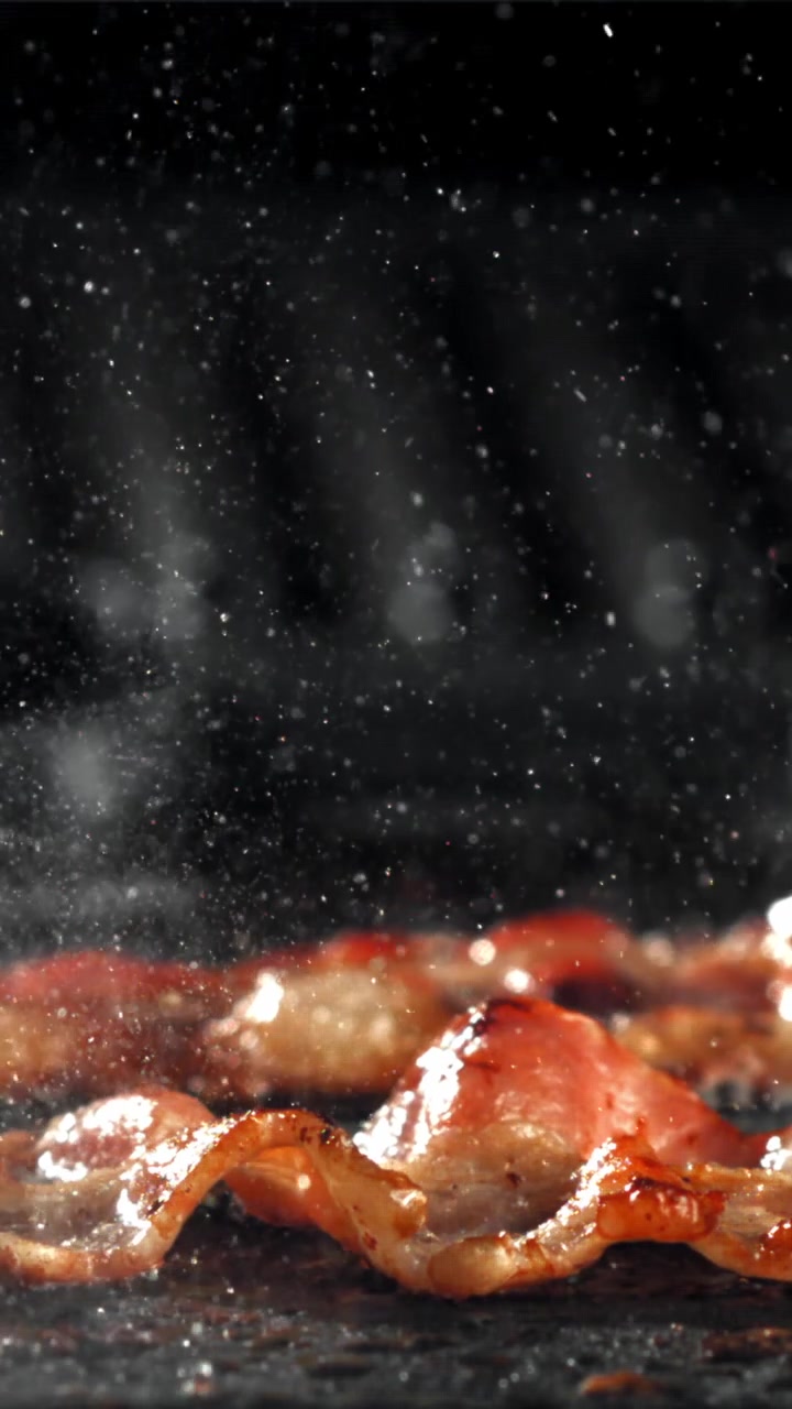 Primo piano di bacon che frigge e sfrigola con schizzi di grasso