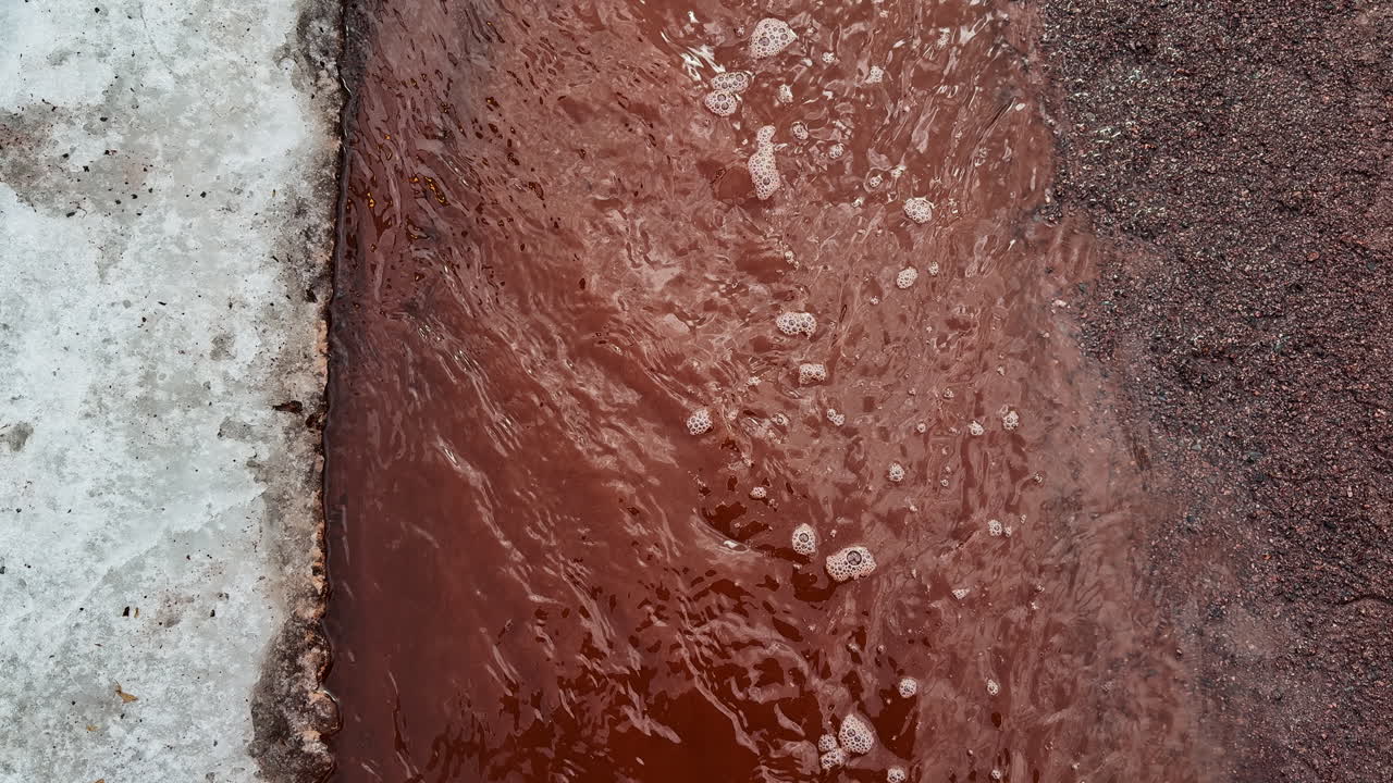 Abbondante acqua di disgelo scorre tra la neve persistente e la terra rossa che si sta scongelando, creando una scena di fine inverno riccamente strutturata dove la primavera inizia a prendere il sopravvento.