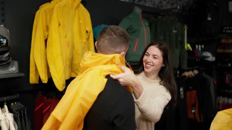 mujer tratando con su hombre chaqueta de lluvia en la tienda de ropa, burlándose