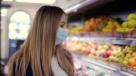 woman in protective mask looking for fruits in supermarket