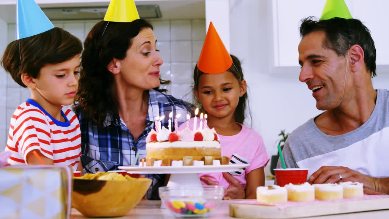Family at table mom cheering girl blowing cake candles for party ad, confetti animating over faces