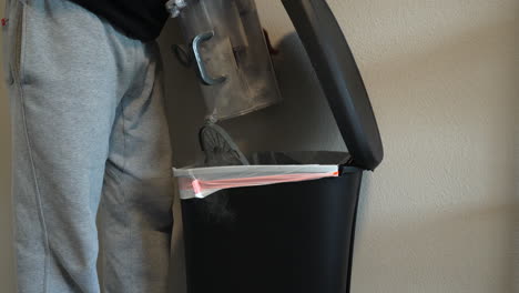 man emptying full vacuum canister into a flip top garbage can and producing dust in the air