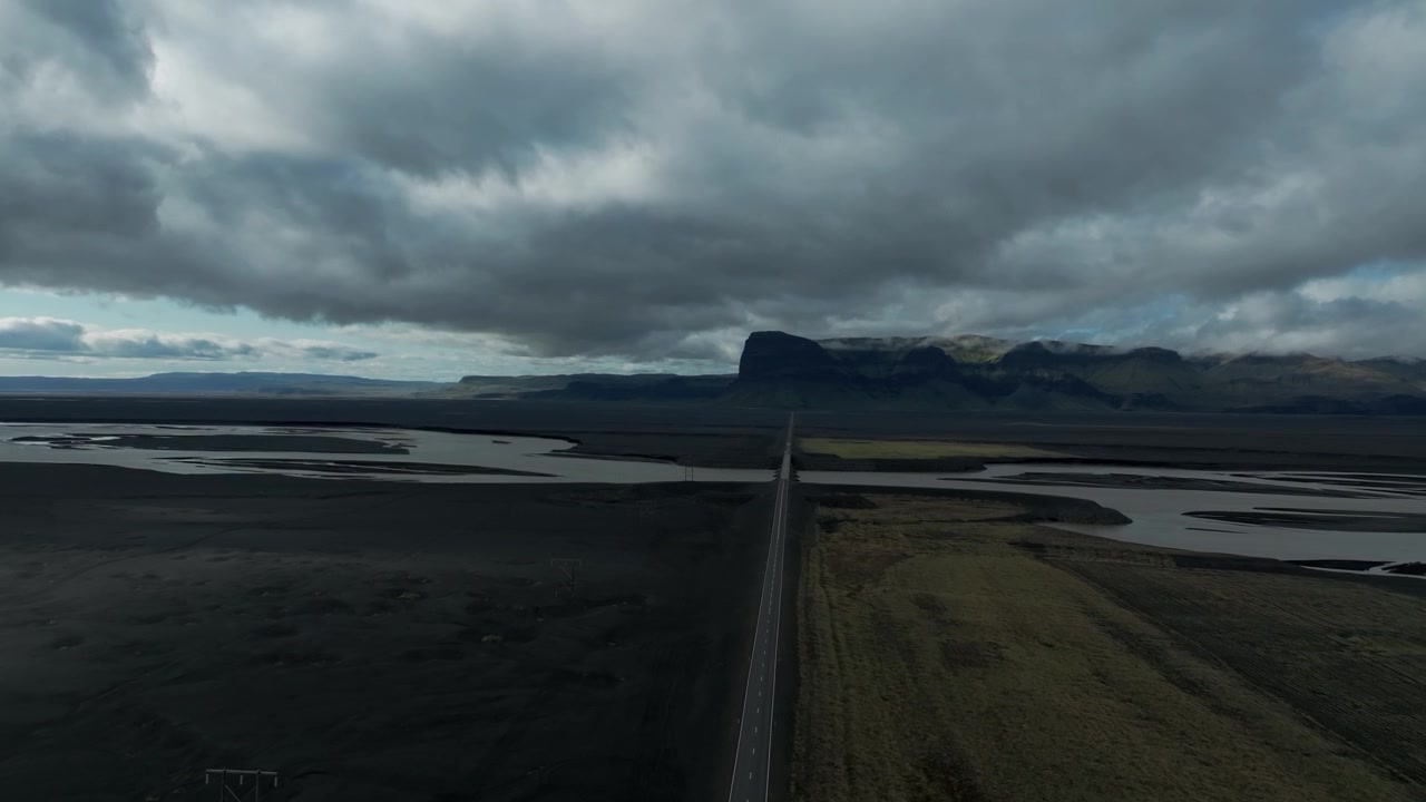 Flying Above The Ring Road In South Iceland With View Of Lomagnupur Mountain With Low-hanging Clouds In Distance. wide aerial shot
