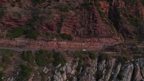 coche viajando en chapman's peak drive después de la puesta del sol en ciudad del cabo, sudáfrica - toma aérea de dron