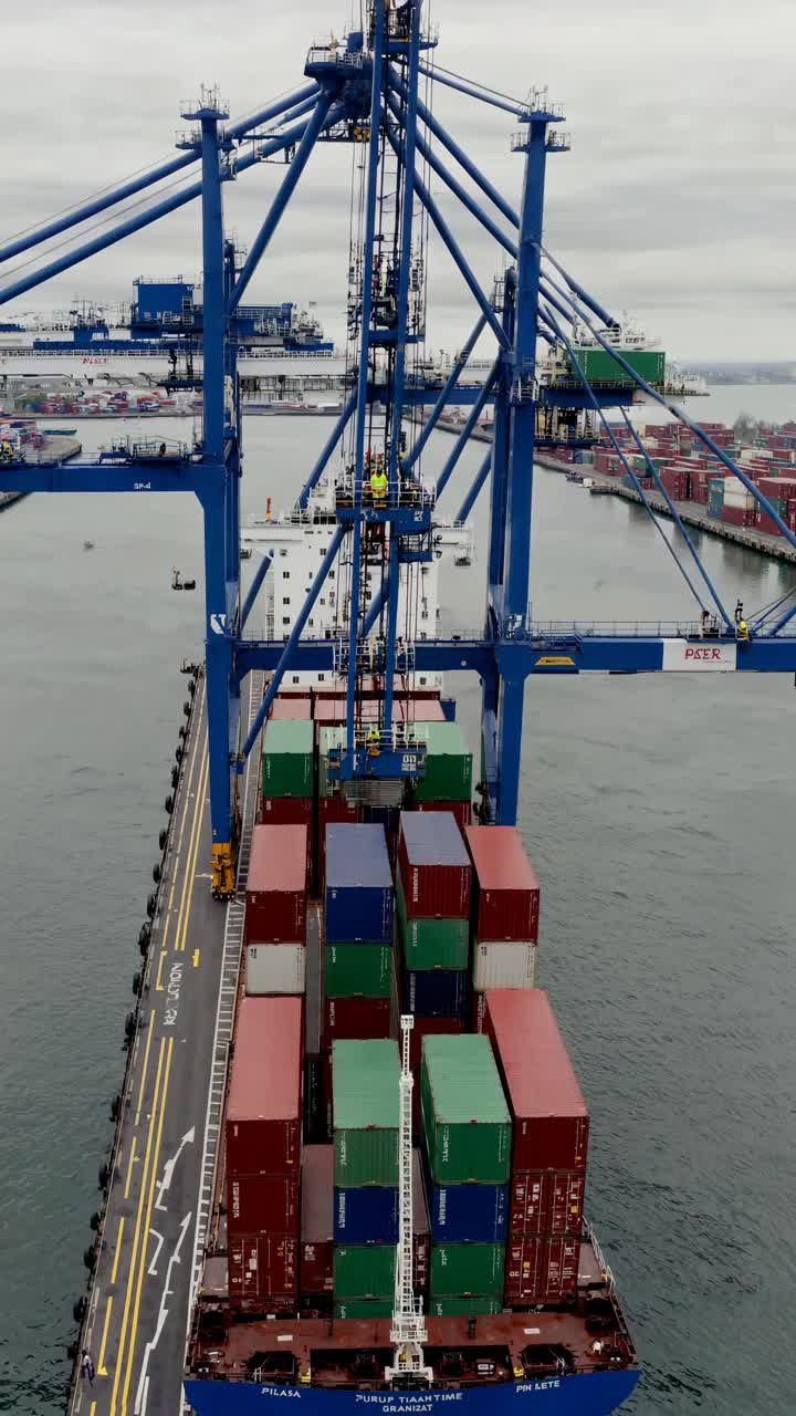 Aerial view video of a cargo ship being loaded with containers at a port, showcasing industrial
