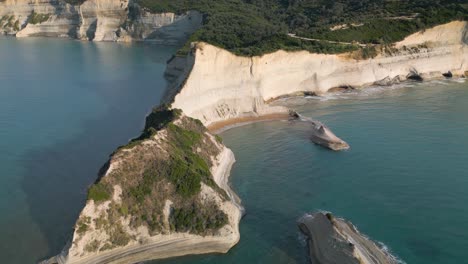 backwards drone shot reveals beautiful cape drastis in corfu, greece golden hour