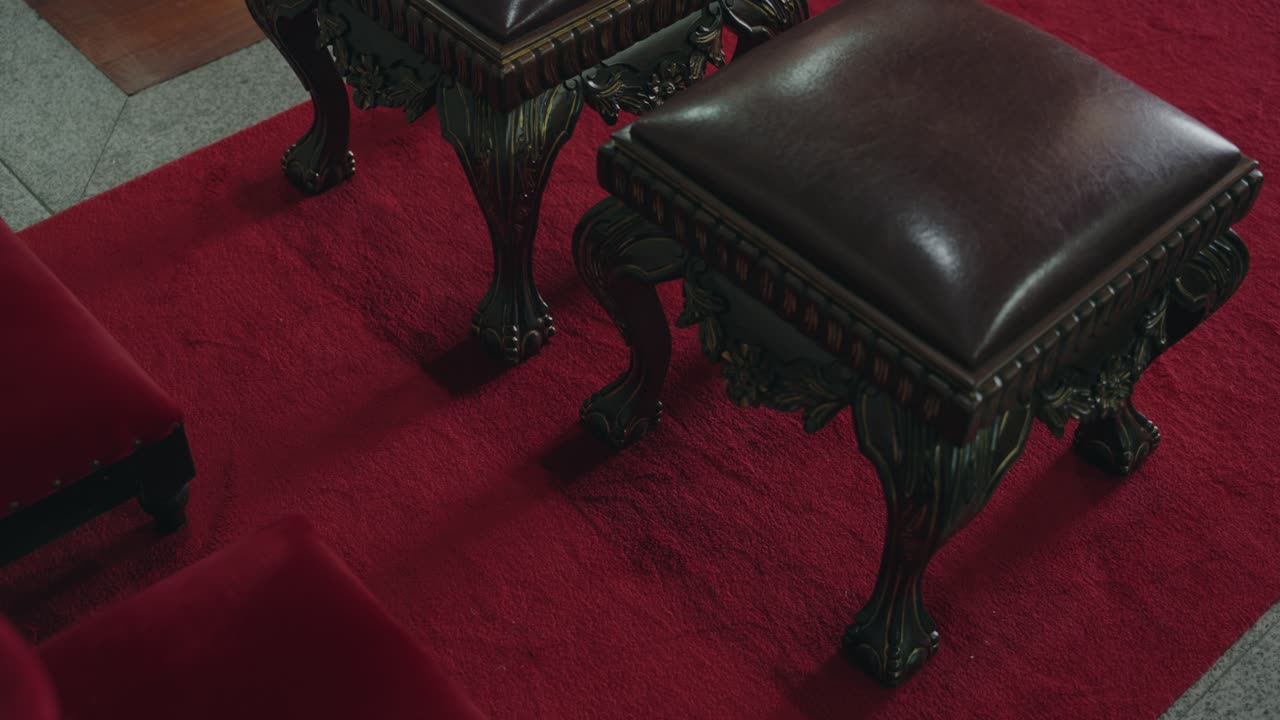 Elegant antique stools with carved legs and leather seats on red carpet