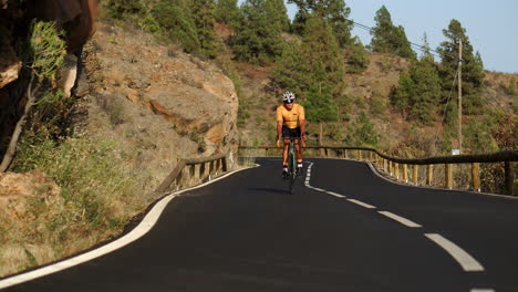 un tipo con una camiseta amarilla está en bicicleta en una bicicleta de carretera deportiva a lo largo de una carretera situada a una gran altitud en las montañas