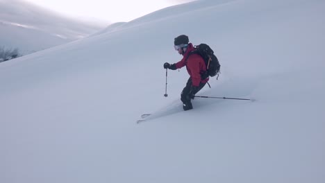 Slow-motion-shot-of-a-man-wearing-red-jacket,-skiing-downhill,-surrounded-by-snow-white-mountain-and-semi-sunny-background-covered-with-clouds