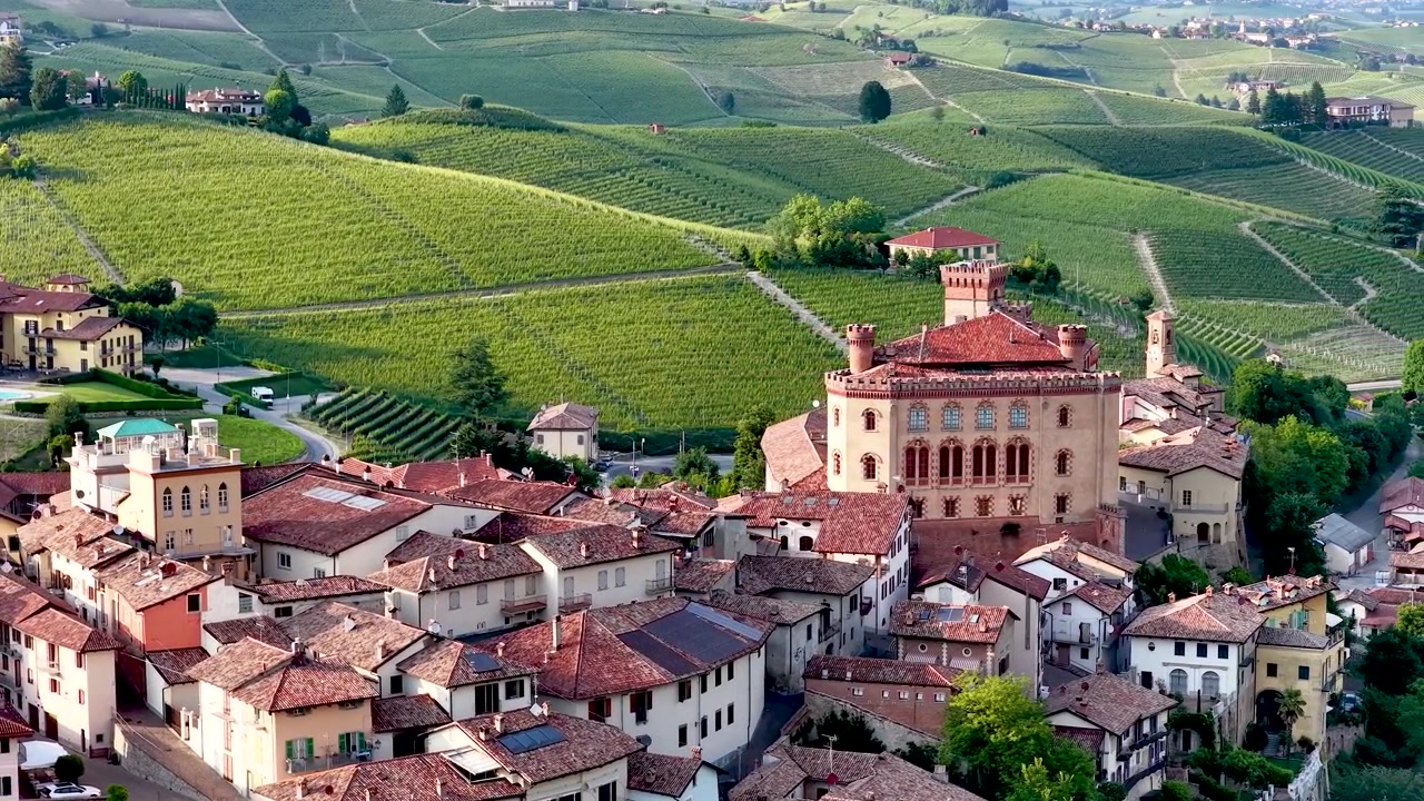 Una ripresa aerea con drone cattura un borgo storico italiano e un castello tra vigneti ondulati.