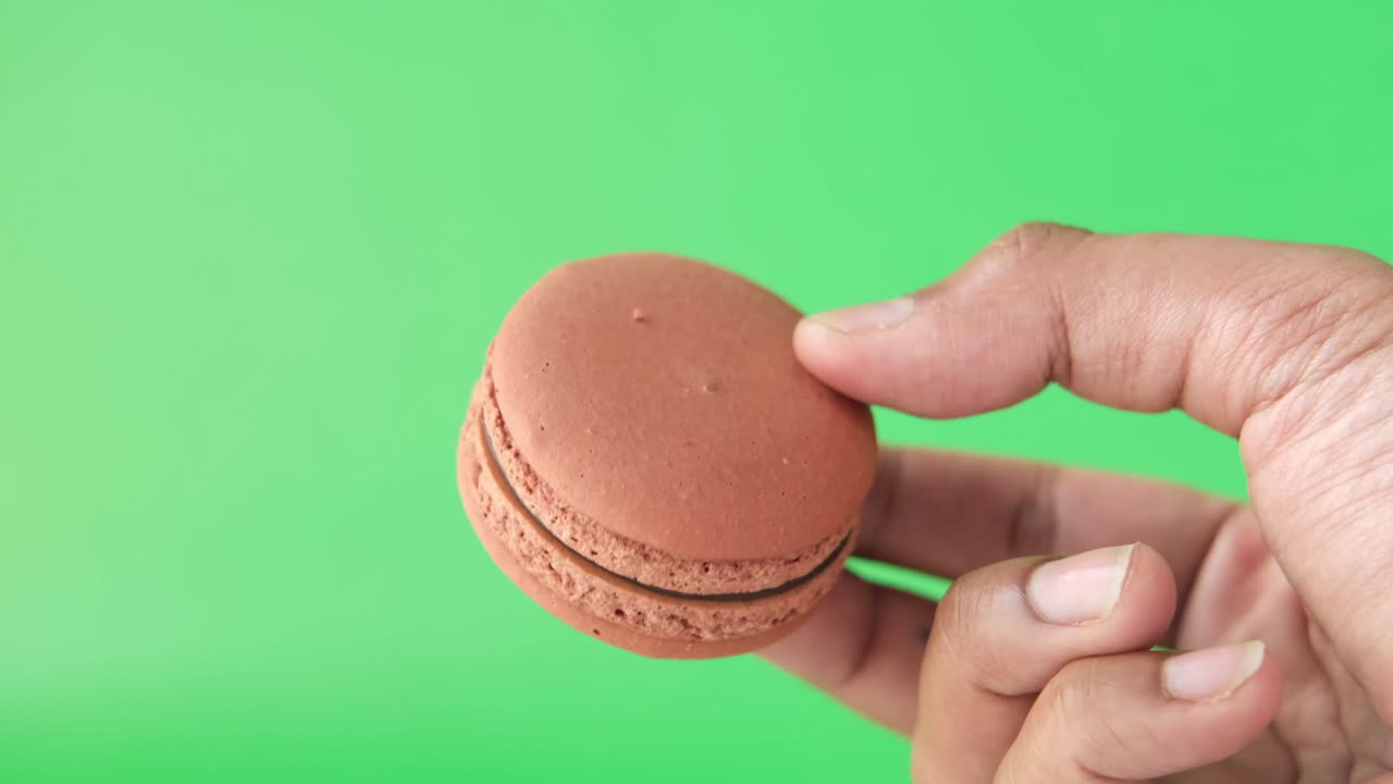 mano sosteniendo macarrón contra fondo verde de cerca