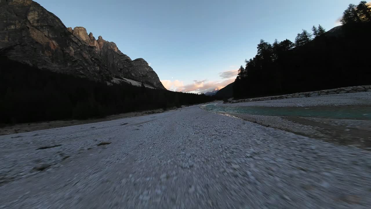low flying aerial footage over a mountain riverbank in Switzerland at sunset dusk, with an adventurous, dynamic nature feel