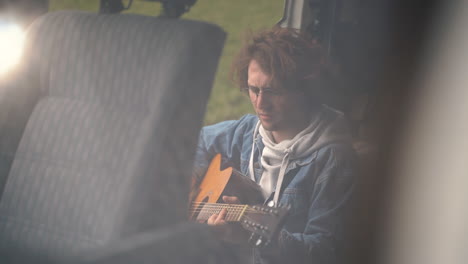 Un-Joven-Con-Gafas-Toca-La-Guitarra-En-La-Parte-Trasera-De-Una-Caravana-1