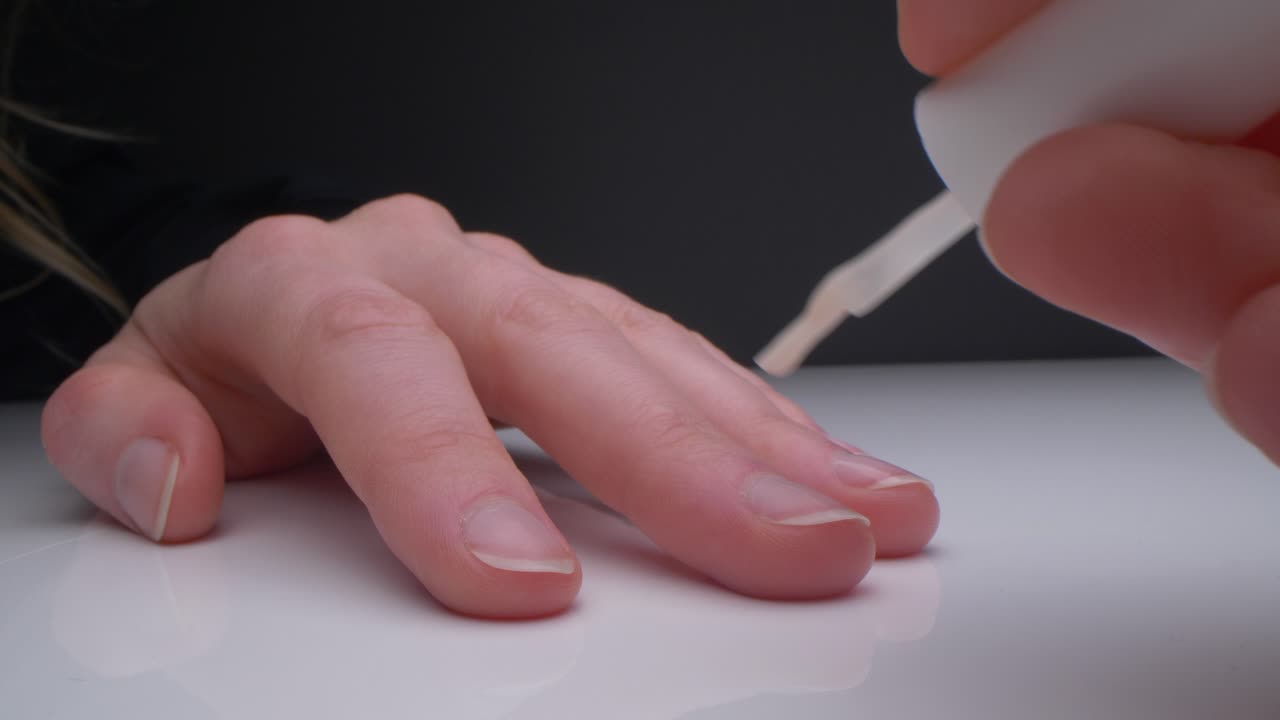 vista de cámara macro de mujer pintando sus propias uñas con esmalte de uñas transparente