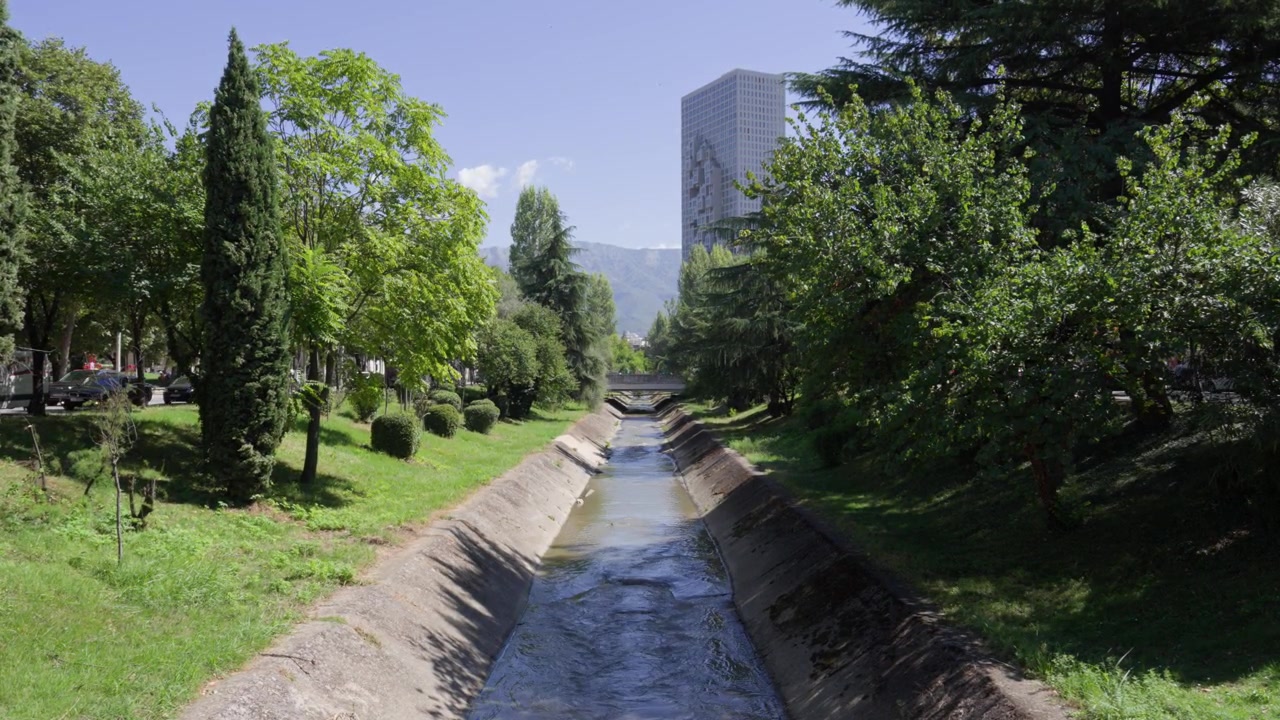 Vista urbana escénica de un canal de río de hormigón bordeado de árboles verdes en Albania