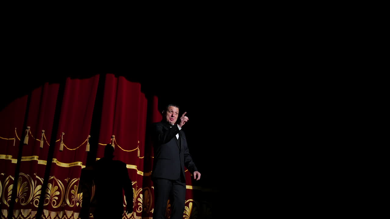 Senior man in costume on stage in darkness. Actor man in selective light on stage during the performance in the theater.