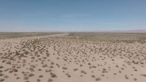 vasta arena del desierto, toma aérea de drones del paisaje desértico y arbustos con cielo azul arriba