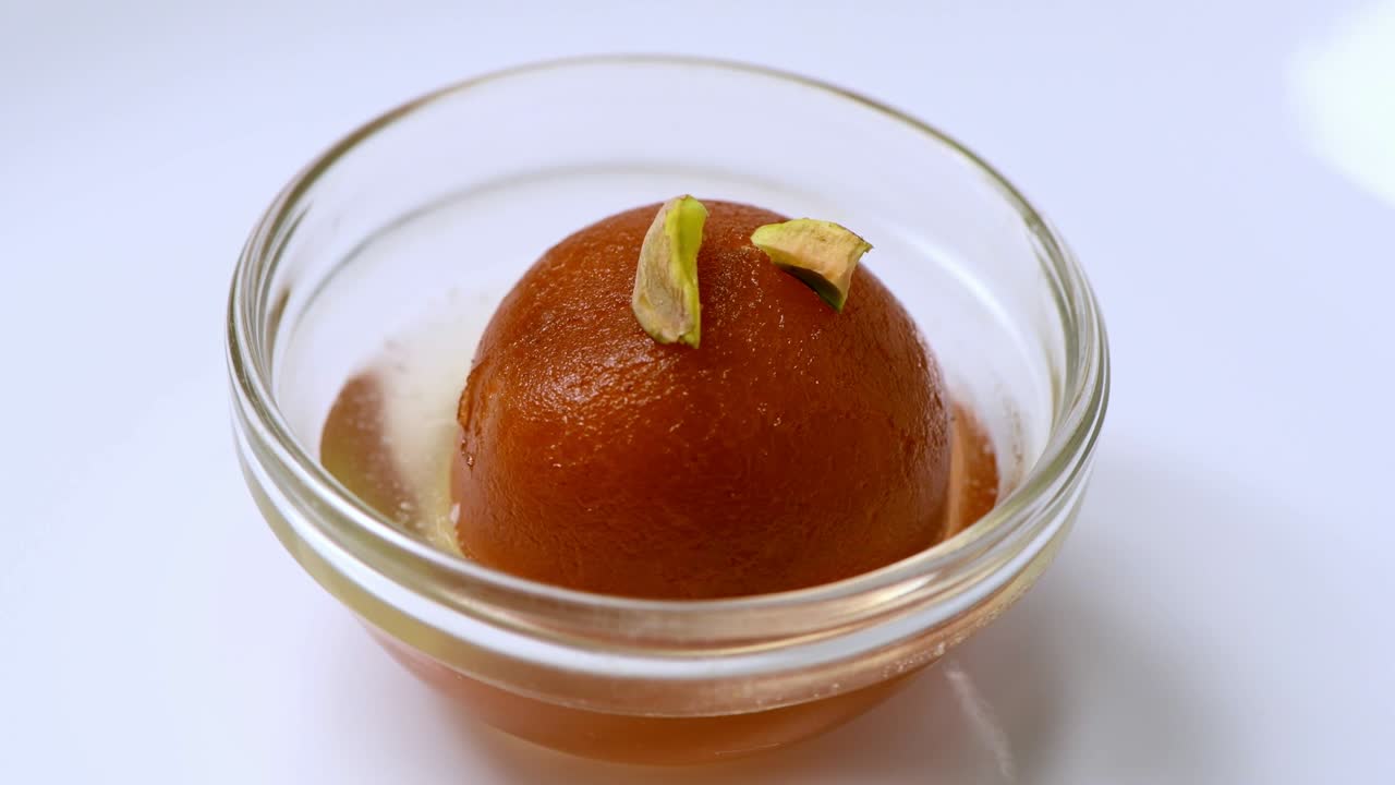 Gulab jamun che ruota con granella di pistacchio (dolce indiano) | Dessert in ciotola di vetro