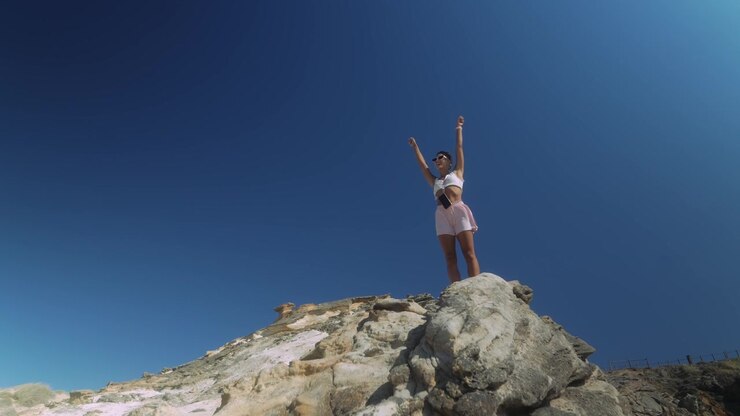Giovane donna in piedi sulla cima di una scogliera rocciosa contro un cielo azzurro limpido