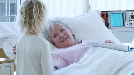 senior woman lying in bed in hospital talking to a little girl