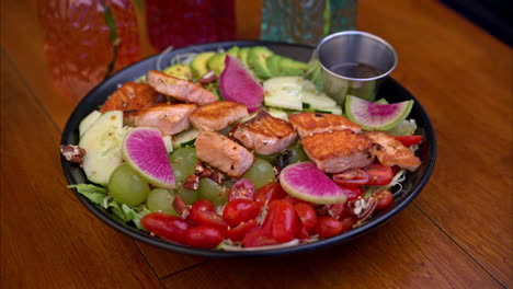 pull back shot of a plate with a healthy snack with grilled salmon tomatoes grapes cucumbers radish and other vegetables