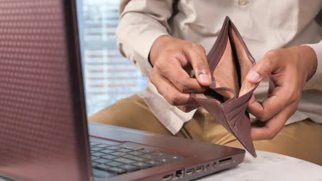 hombre con la billetera vacía delante de la computadora portátil