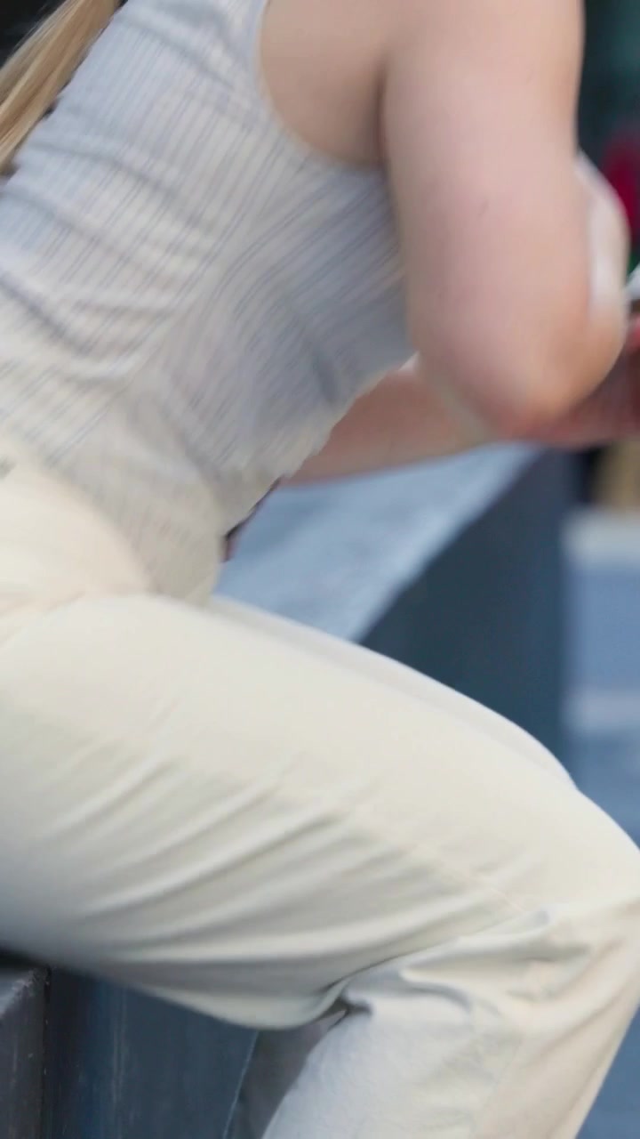 Vertical video: Reaching into bag, woman on ledge in tank top scrolling phone, holding cup, walking