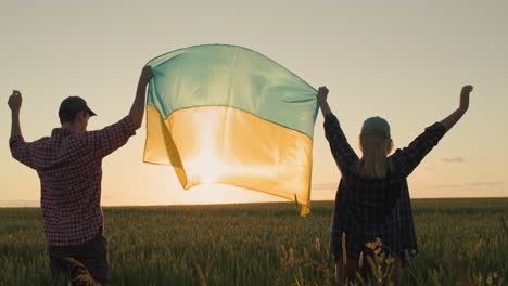 happy ukrainian couple raising the flag of ukraine over a field of wheat at sunset