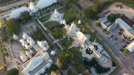 aerial drone of wat rong khun stunning buddhist white temple and golden temple with mountains and landscape in chiang rai, thailand