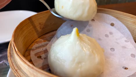 Picking-up-a-tasty-hot-soft-steam-bun-filled-with-coconut-cream,-custard-cream-dessert,-traditional-Asian-food-at-a-restaurant,-4K-shot