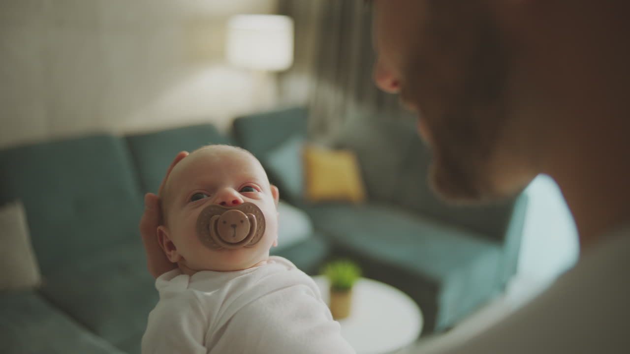 Father holding newborn baby with pacifier in living room