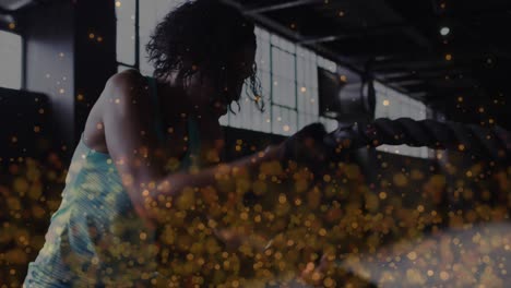 Animation-of-golden-dots-floating-over-woman-exercising-with-ropes-in-an-abandoned-building