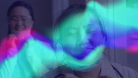 animation of green, blue and pink waves over happy asian women taking off face mask