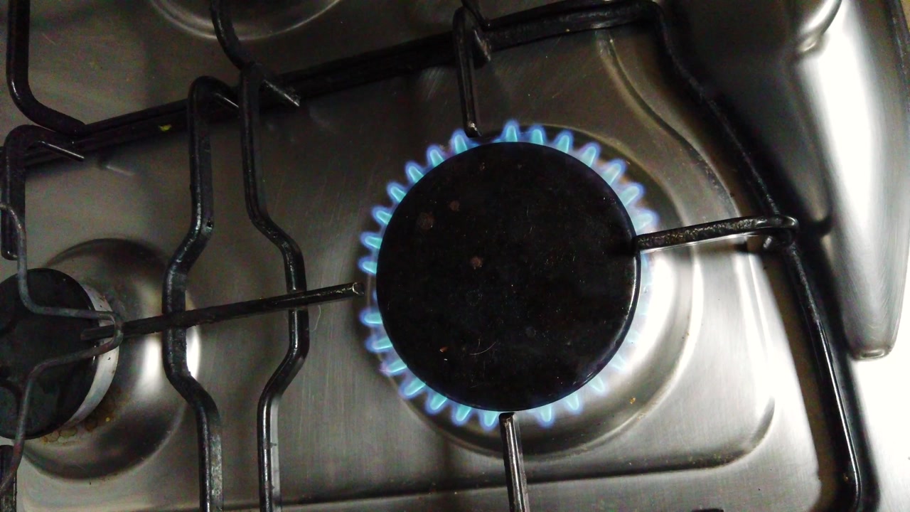 Overhead view of a gas ring on a stove, showing cooking in progress with a bright flame. Perfect for kitchen scenes, food preparation, recipe videos, and culinary backgrounds. Ideal for cooking tutori