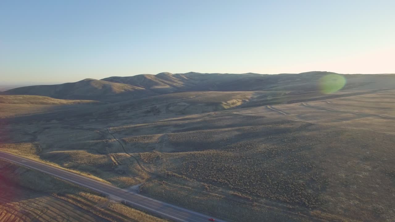 Aerial shot of a car moving across a highway in the desert during sunrise.