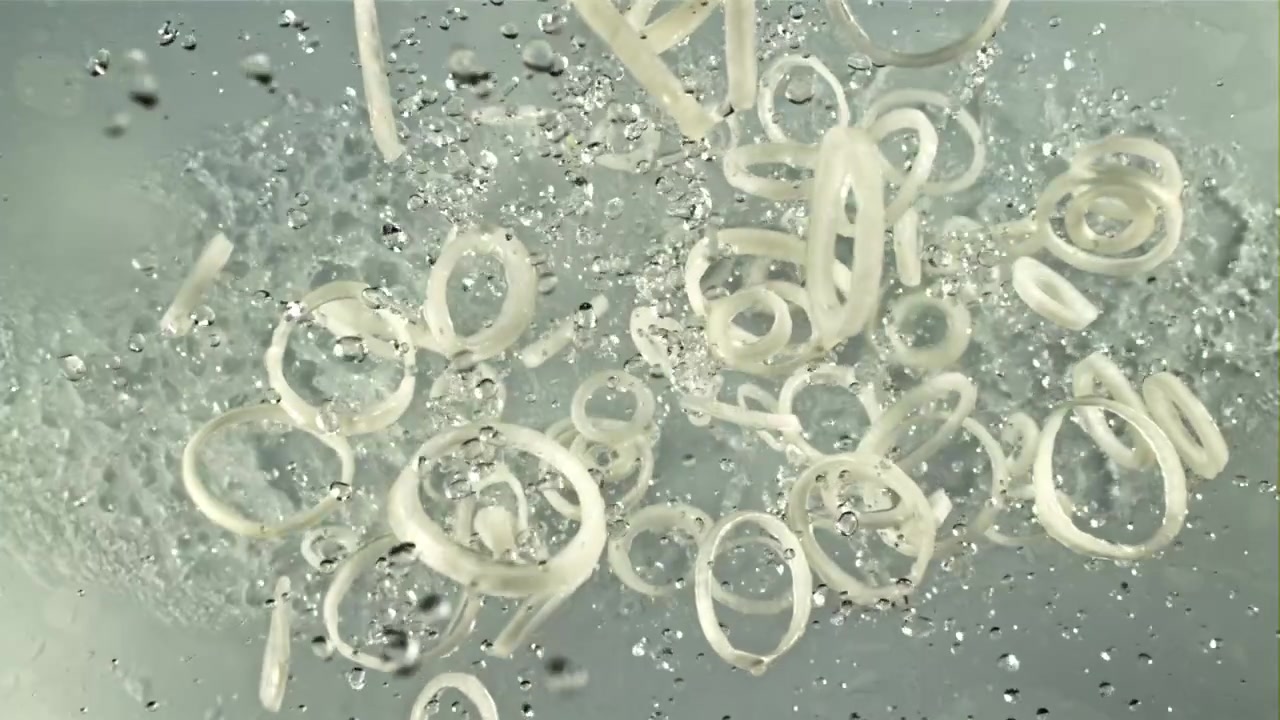 Friske løgringe falder ned i klart vand i slowmotion